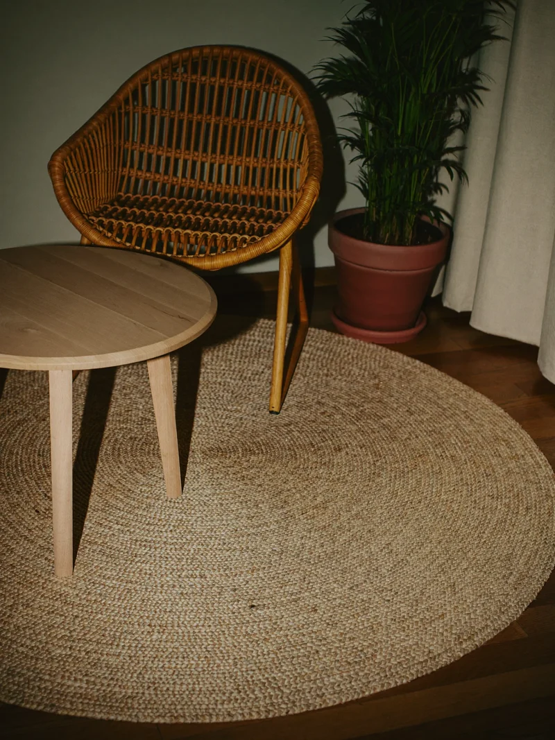 Runder Jute-Baumwoll-Teppich unter kleinem Tisch und Rattanstuhl in der Leseecke